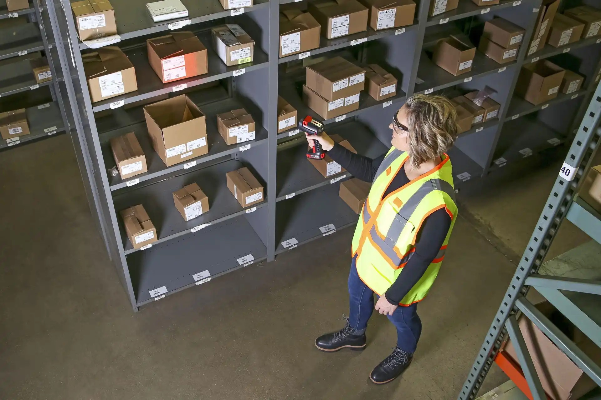 Raktári dolgozó kézi vonalkódolvasóval készletellenőrzést végez polcrendszeren, ipari környezetben